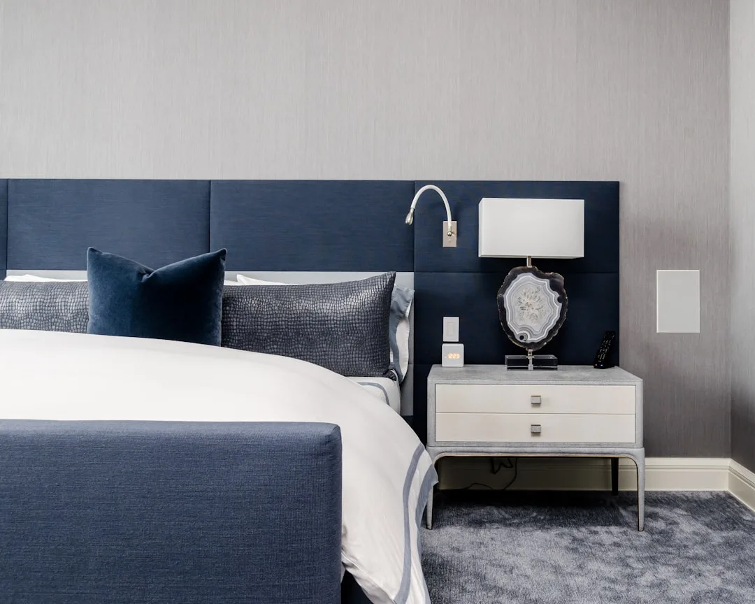 Navy blue upholstered bed with padded headboard wall panel, white bedding, and gray nightstand in modern bedroom