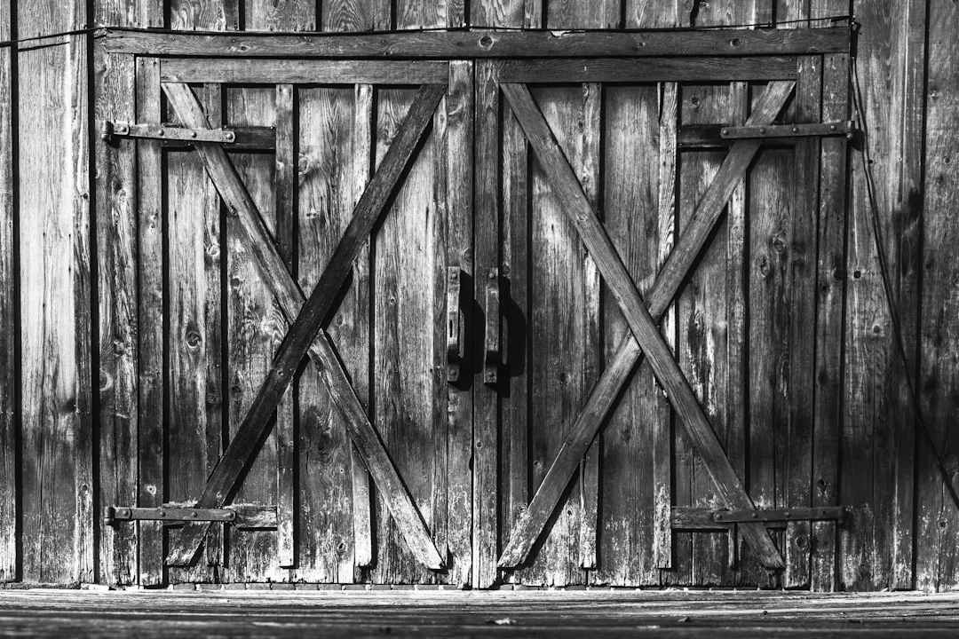 Rustic weathered wooden barn doors with X-brace cross pattern and iron hardware in black and white photography