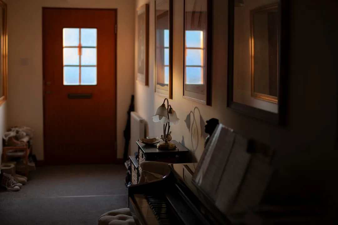 Narrow hallway entryway with upright piano, decorative lamp, framed art and wooden front door with glass panels