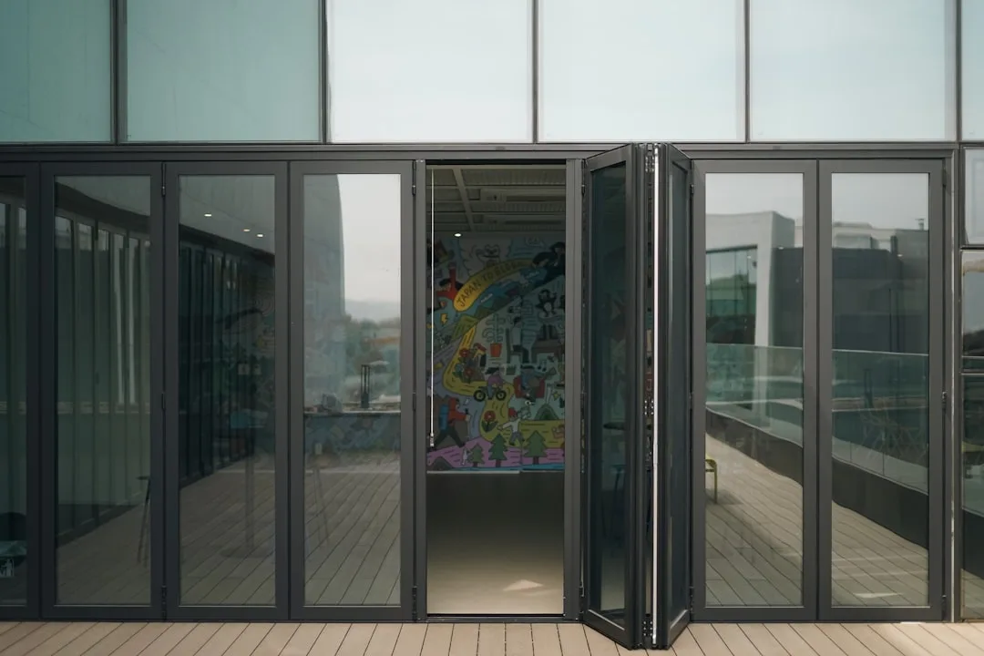Black aluminum bifold doors partially open on a modern building terrace revealing colorful interior mural