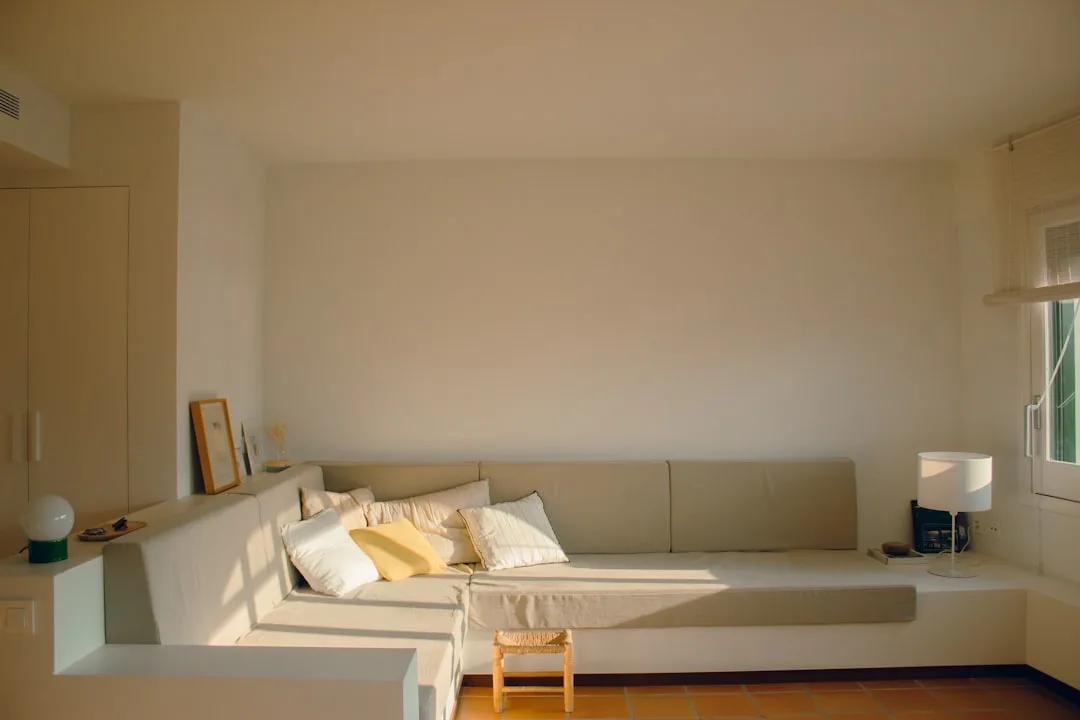 Corner built-in sofa with white cushions in minimalist living room using corner wall geometry efficiently