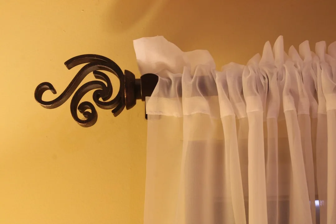 White sheer curtains hung with rod pocket style on decorative bronze curtain rod finial against yellow wall