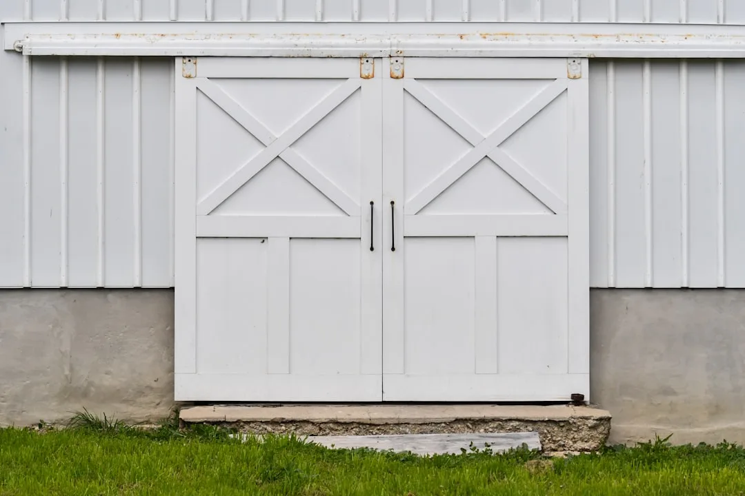 White sliding barn doors with X-pattern panels on a white metal building exterior with green grass