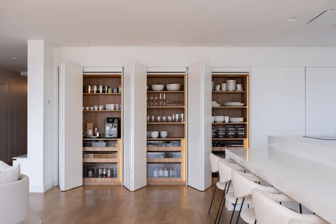 Built-in floor-to-ceiling pantry cabinets with fold-out doors revealing organized shelves with dishes and appliances