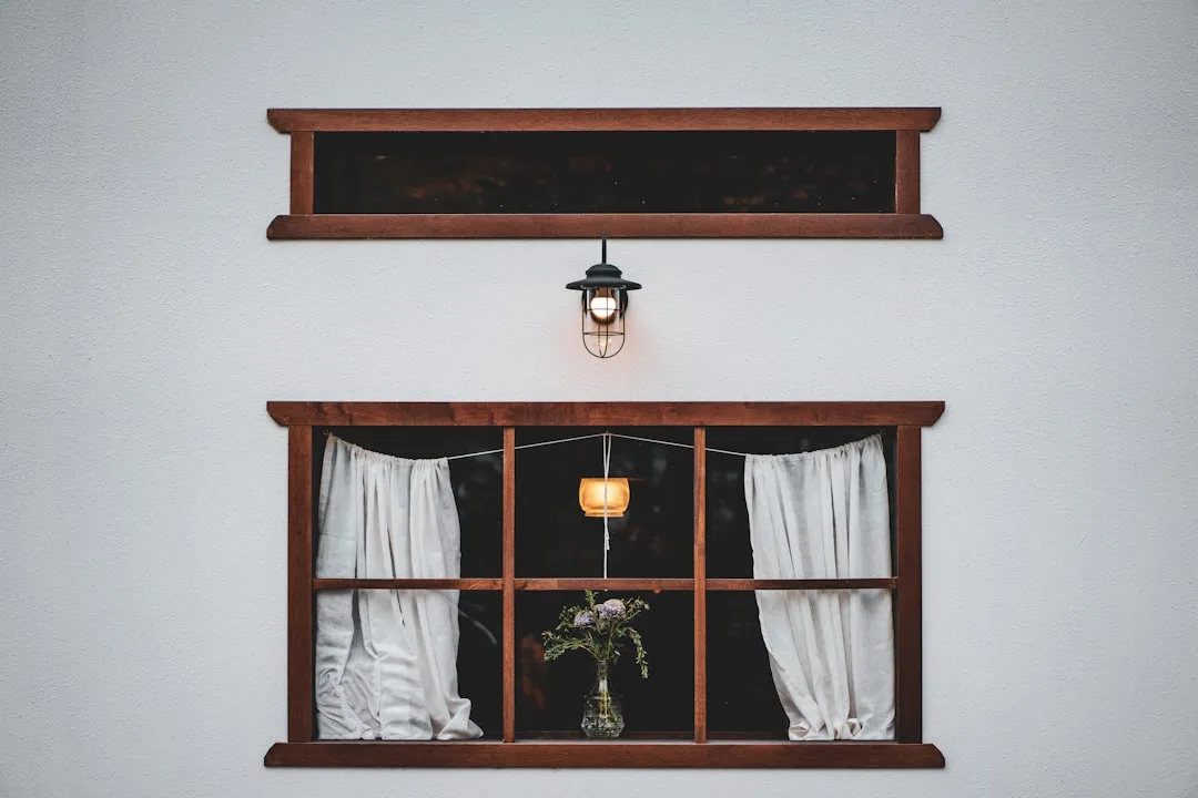Rustic wooden window nook with white curtains, hanging lantern, and flower vase borrowing natural light as design elemen