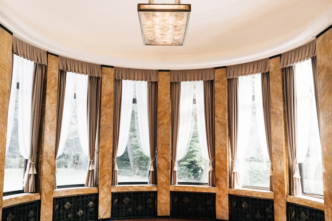 Ceiling-hung curtain panels in curved bay window room with layered sheer white and taupe drapes on ceiling-mounted track