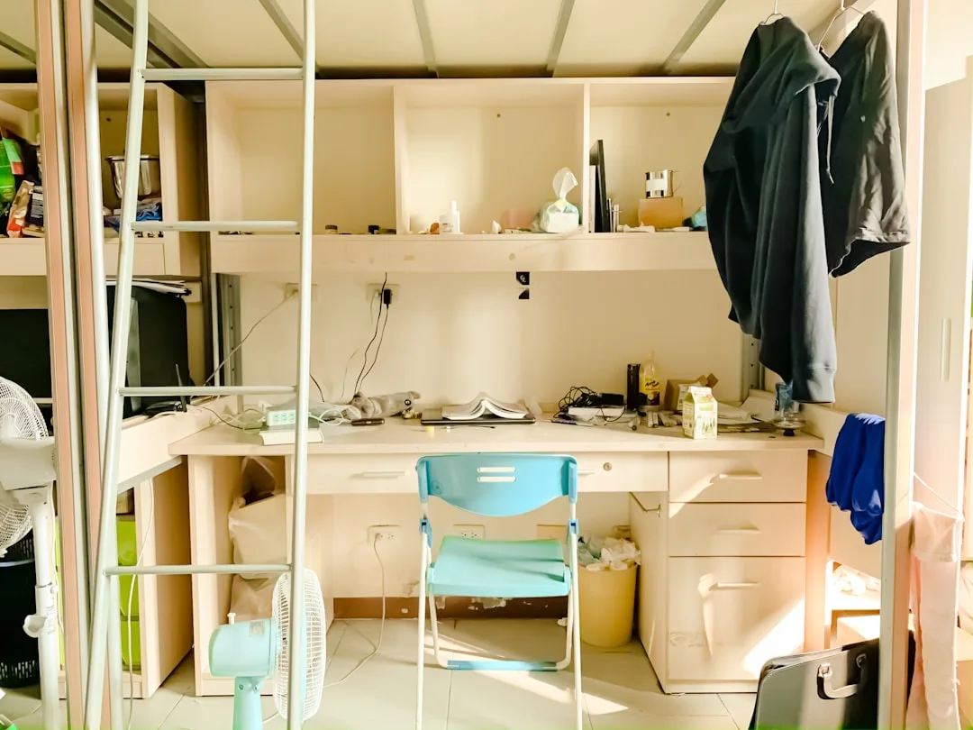Closet converted into built-in desk workstation with shelving, drawers, laptop, and blue folding chair in small room