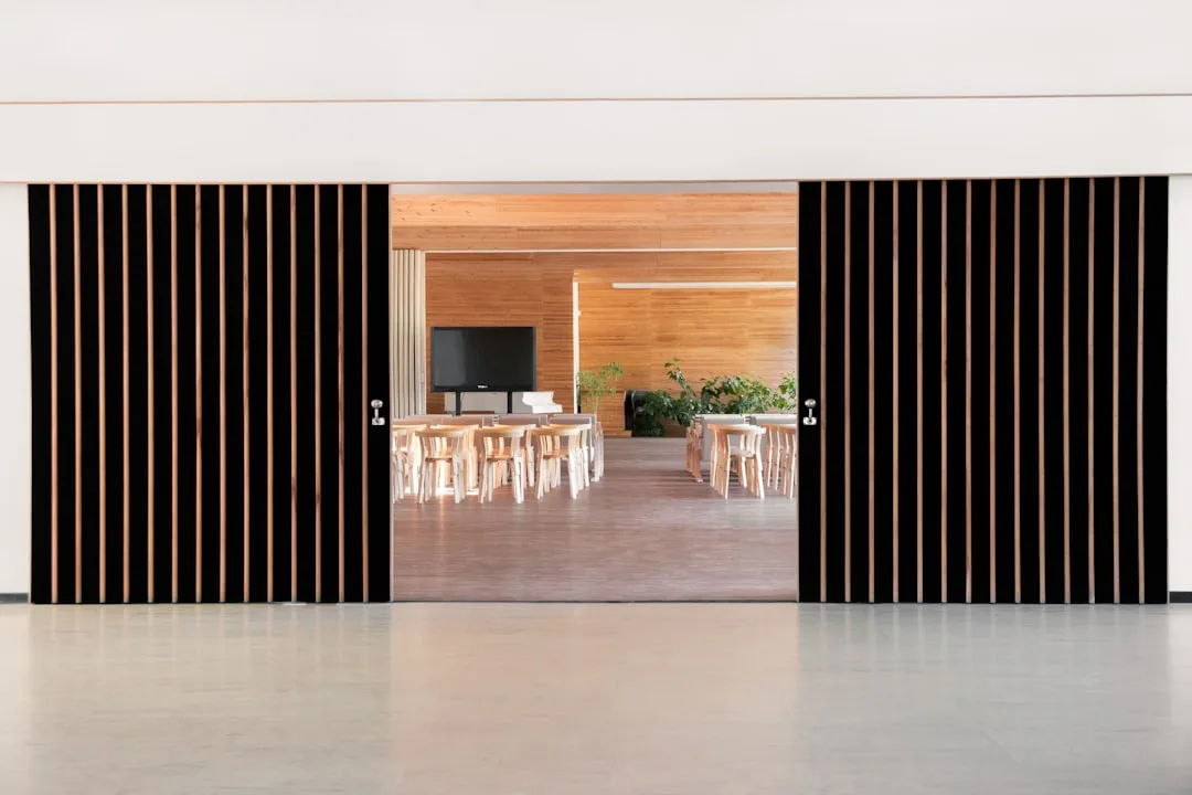 Modern sliding bypass doors with black vertical slat panels opening to a contemporary dining or conference room