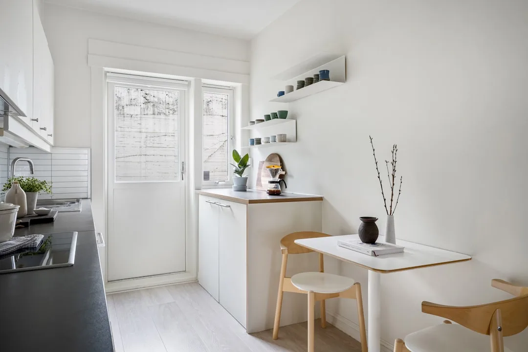 Small Scandinavian kitchen with single-wall layout, white cabinets, wall-mounted fold-down table and wooden chairs