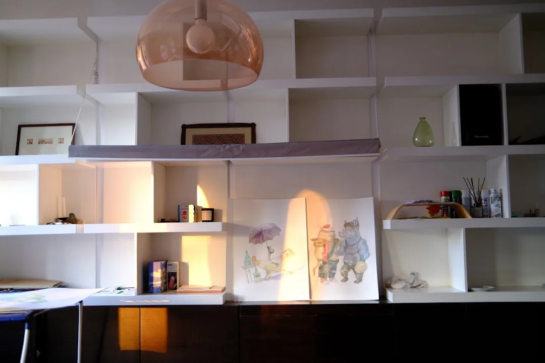 White modular wall shelving unit with multiple open cubbies displaying art supplies, books, and decorative objects