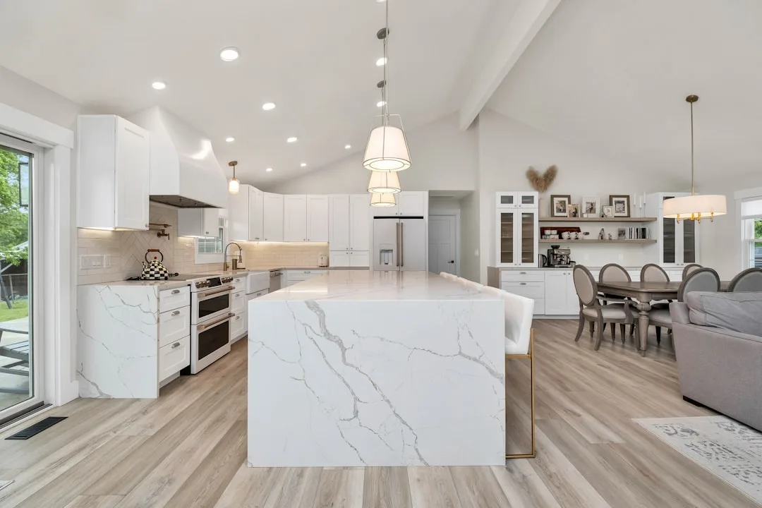 Large marble kitchen island extending toward dining area as open-plan kitchen dining room divider in modern white kitche