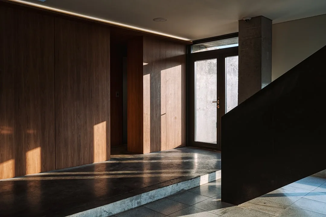 Large pivot door with wood paneling in modern interior with dramatic natural light and concrete flooring