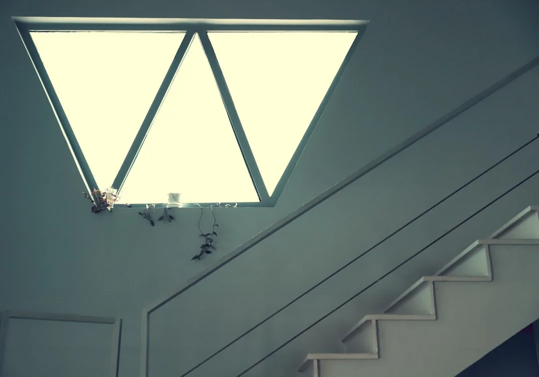 Geometric triangular skylight window above a white staircase with built-in under-stair shelving in modern home