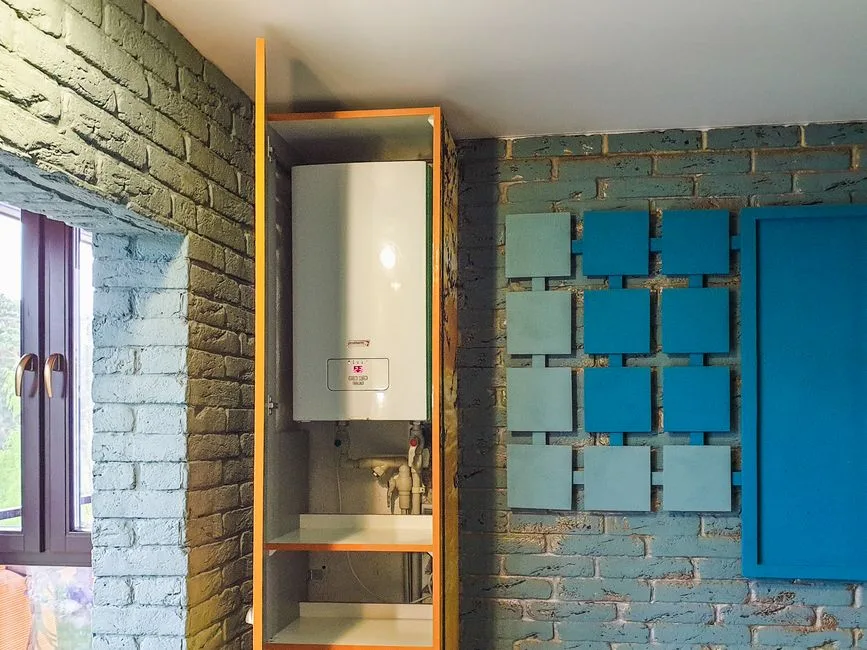 Orange-framed cabinet enclosing a wall-mounted water heater on painted brick wall with blue acoustic panels