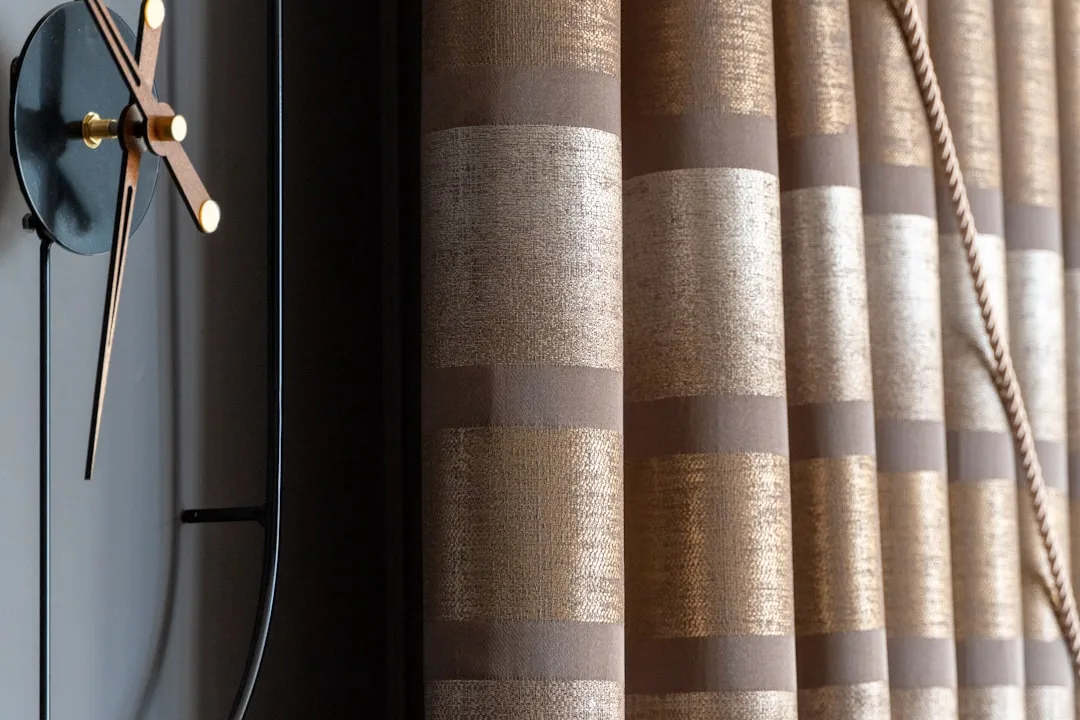 Elegant striped brown and gold fabric curtain panels with decorative rope tieback next to a modern black wall clock