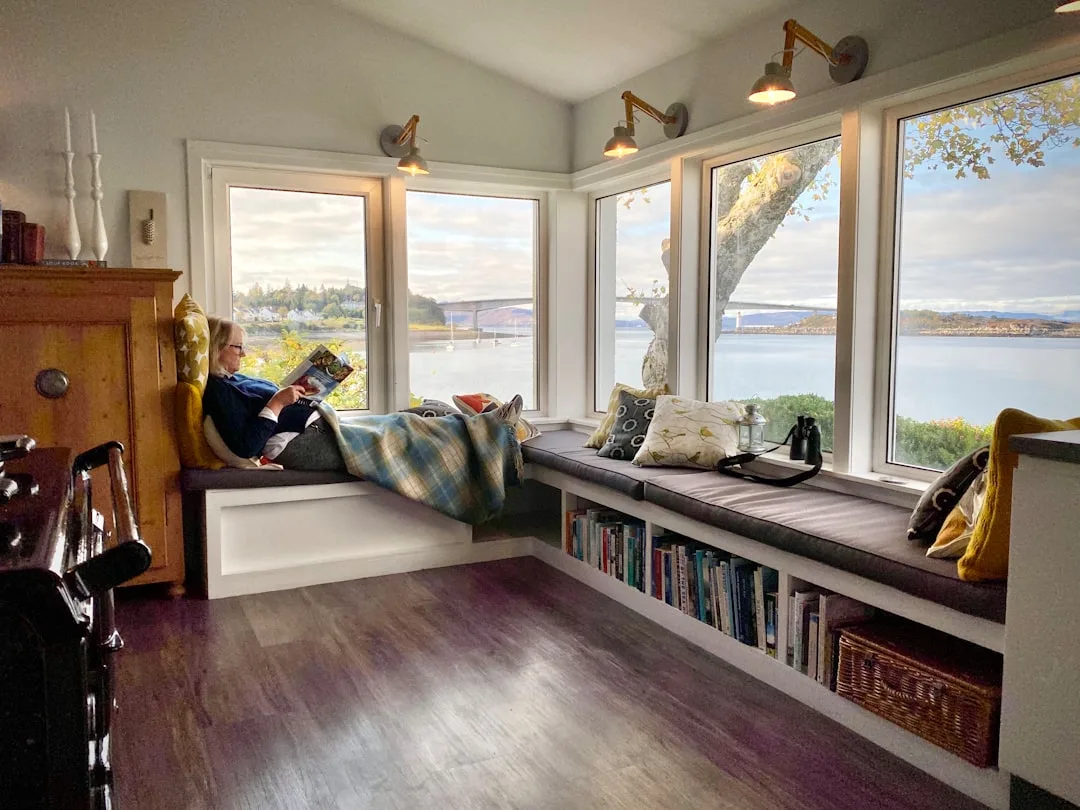 Built-in bay window seat with storage bookshelves, cushions, and waterfront view in a cozy reading nook