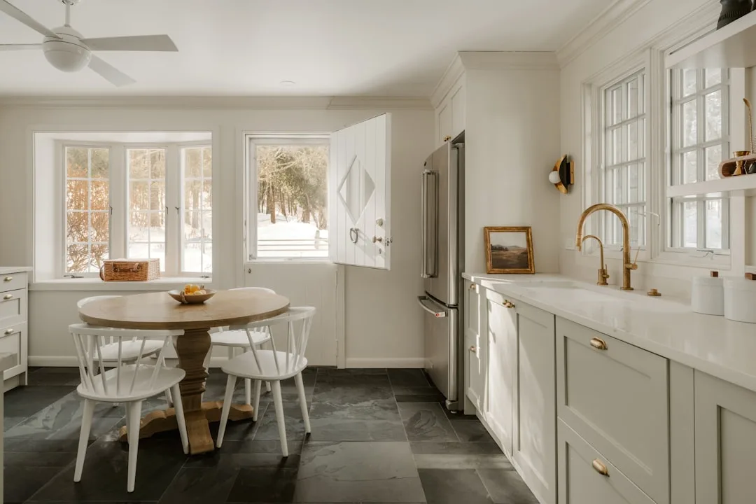 Dutch door with top half open in a bright farmhouse kitchen with white cabinets and slate tile floor