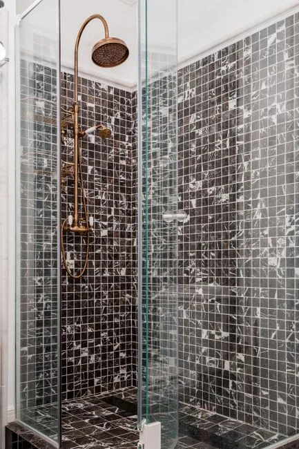 Corner wet room shower with black marble mosaic tiles and brass rainfall showerhead in compact bathroom layout