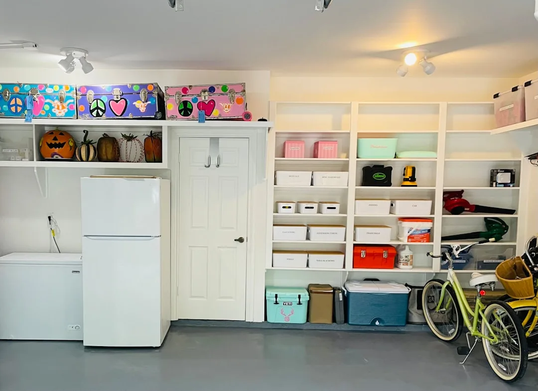 Organized garage with white built-in shelving and overhead wall-adjacent storage displaying colorful trunks and pumpkins