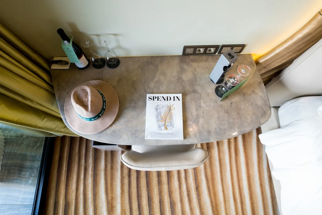 Hotel guest room desk with straw hat, Spend In magazine, wine bottles and glasses on marble table top view