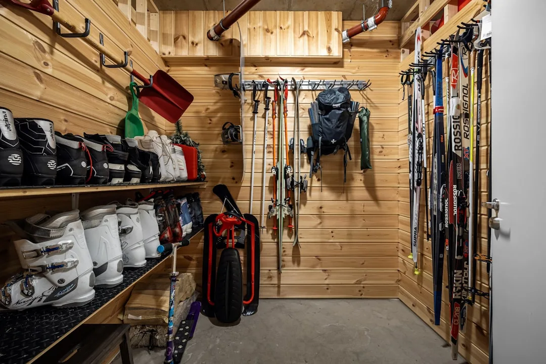 Organized ski gear storage room with shelved ski boots, wall-mounted skis, poles, and backpacks in a wood-paneled space