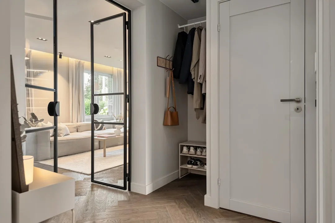 Modern entryway hallway with open coat closet, shoe rack, hanging jackets and leather bag near glass partition door