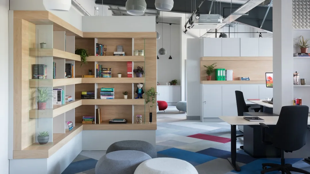 Open-plan office with zoned layout featuring built-in wood shelving, dedicated work desks, and modular storage cabinets