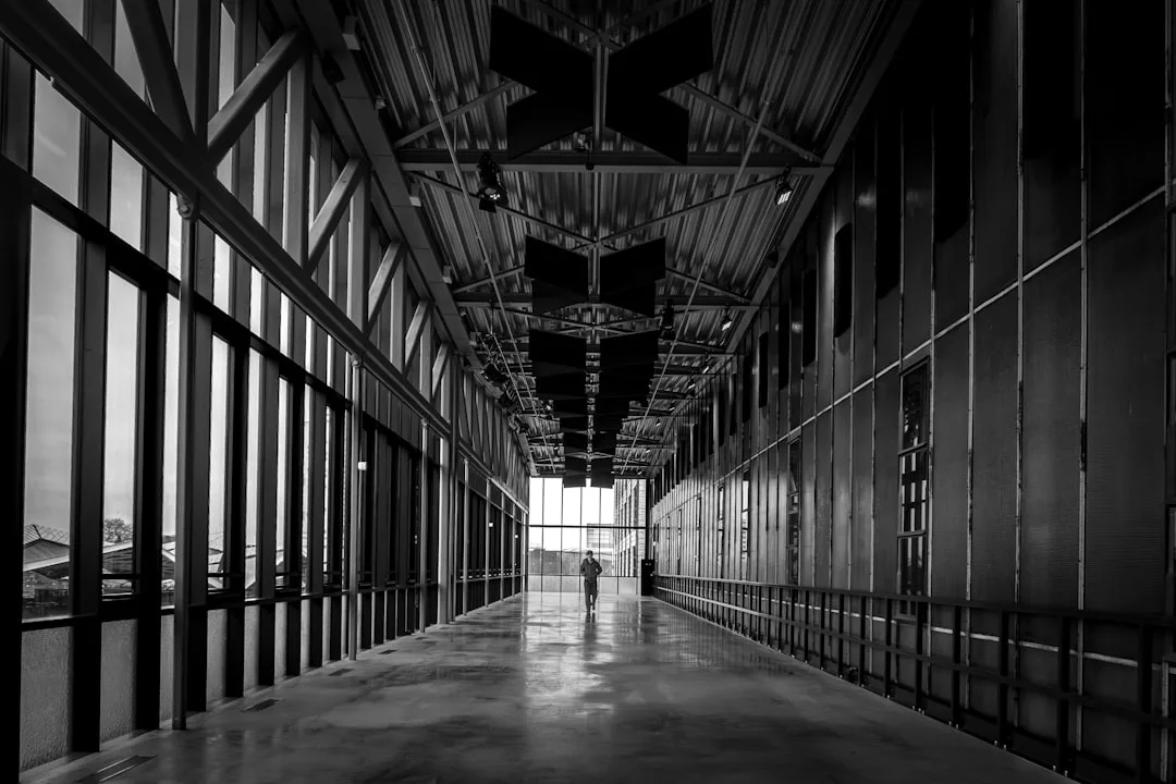 Long architectural hallway with glass walls and exposed steel ceiling showing linear corridor space with reflective conc