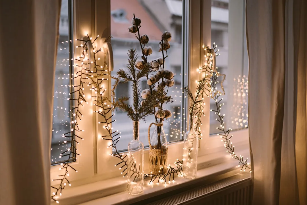 Minimalist window sill decorated with fairy lights, glass bottles, pine sprigs and cotton branches for cozy winter decor