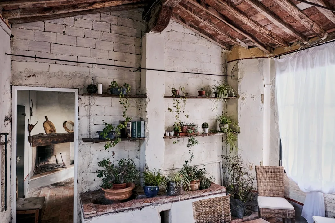 Rustic reclaimed kitchen nook with whitewashed brick walls, wooden shelves with potted plants, and exposed beam ceiling