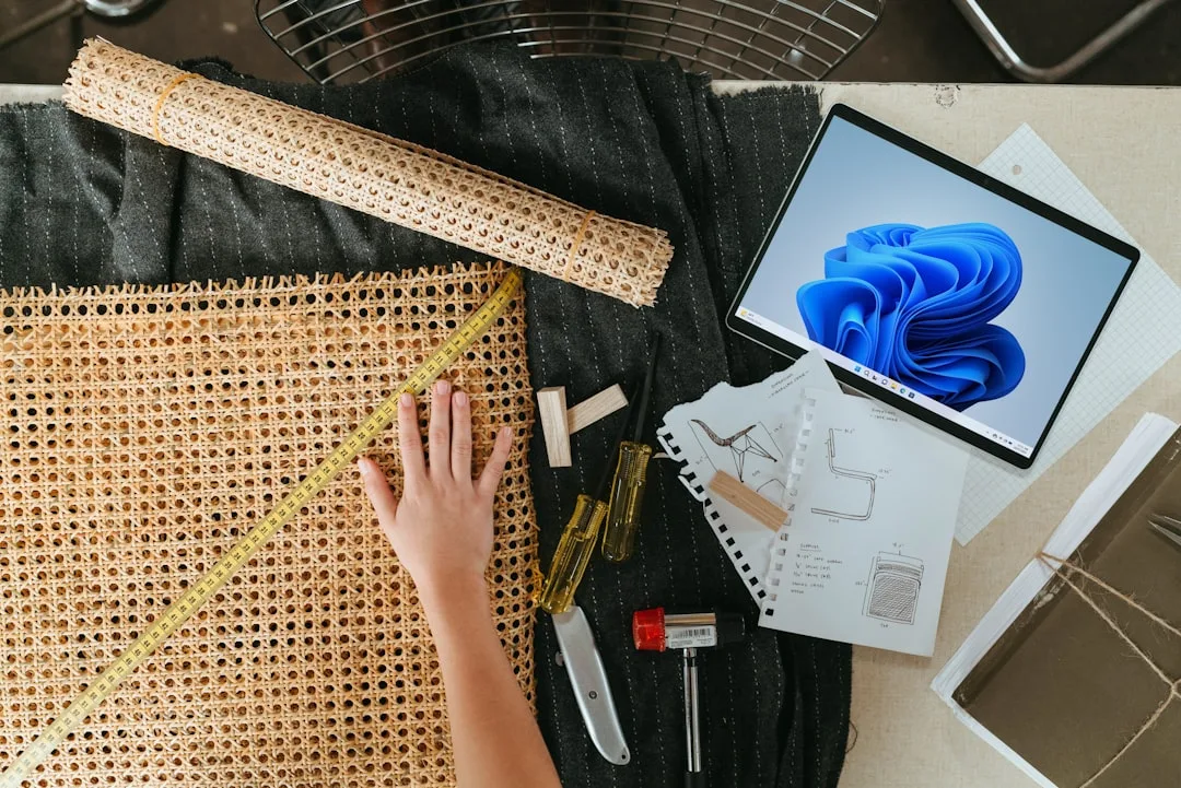 Top-down view of cane webbing material with measuring tape, tools, sketches and tablet showing furniture sizing process