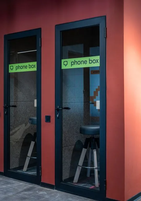 Acoustic phone box pods with glass doors and stools for private calls in open office hallway