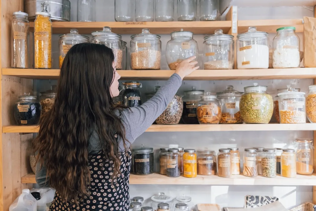 Woman organizing glass jars of dry goods on wooden pantry shelves in a well-designed bulk food storage system
