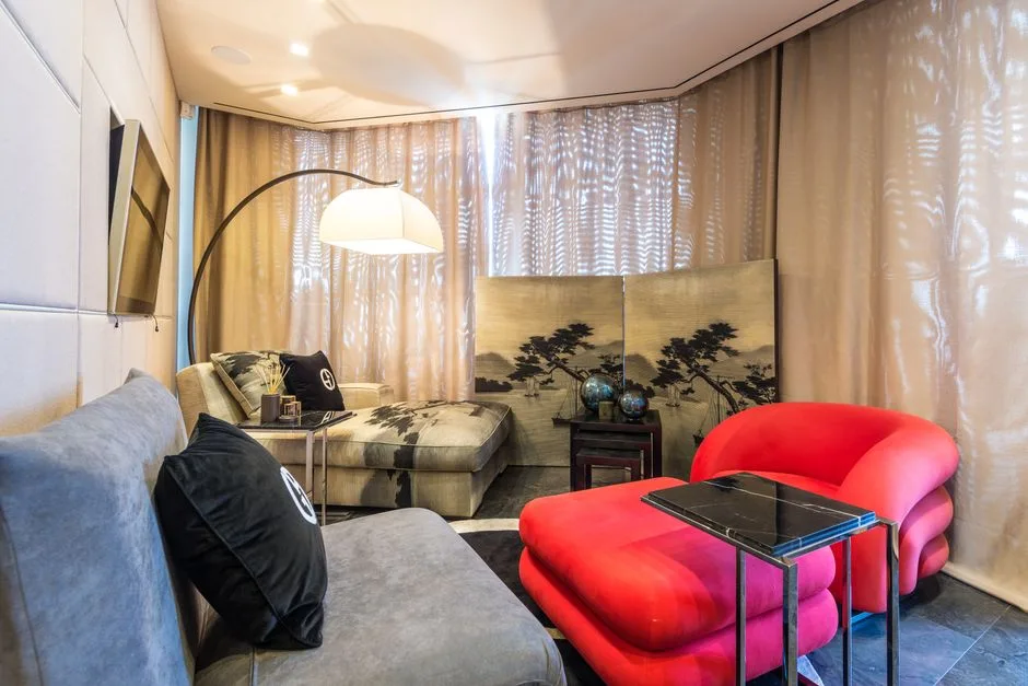 Arc floor lamp placed behind chaise lounge in curved living room with red accent chair and gold curtains