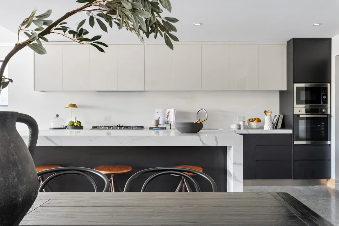 Modern open-concept kitchen with white upper cabinets, dark lower units, marble island, and bar stools in a contemporary