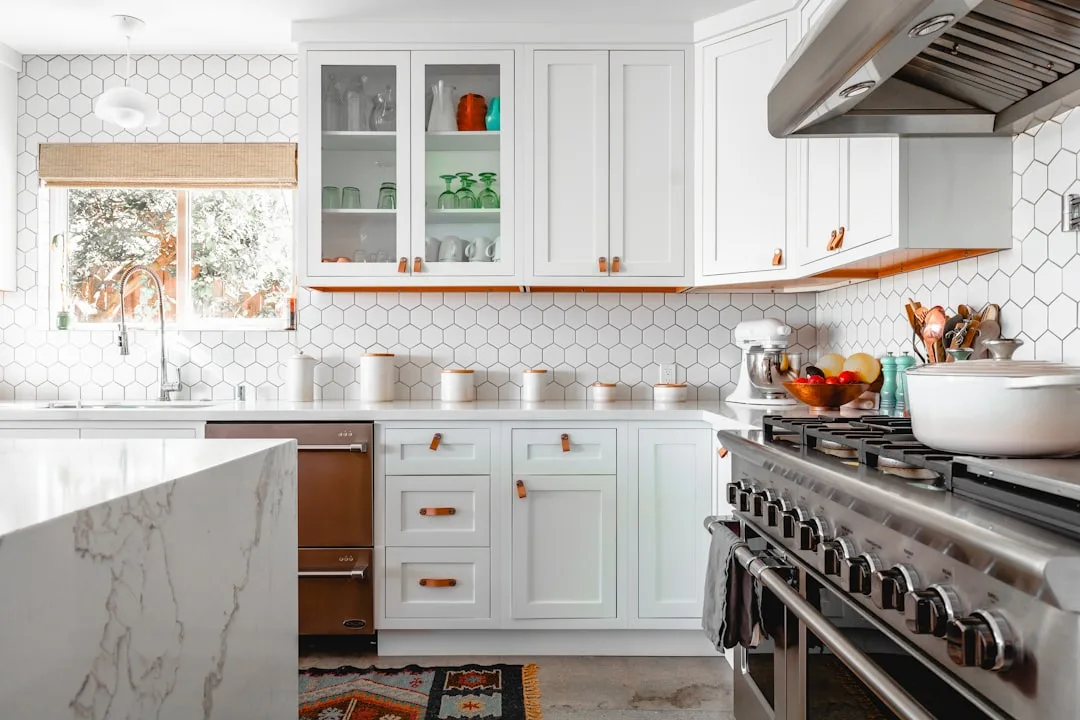 Bright white kitchen with open glass cabinets showing organized glassware, white shaker cabinets with leather pulls, hex