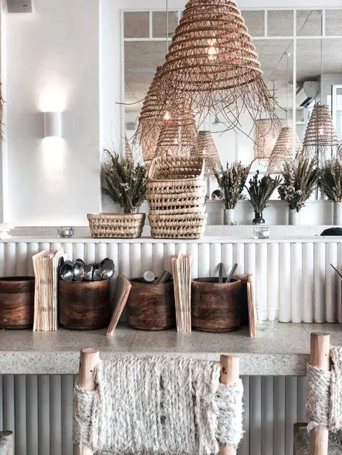 Woven baskets and wooden bins organizing cutlery and menus on a boho restaurant counter with rattan pendant lights