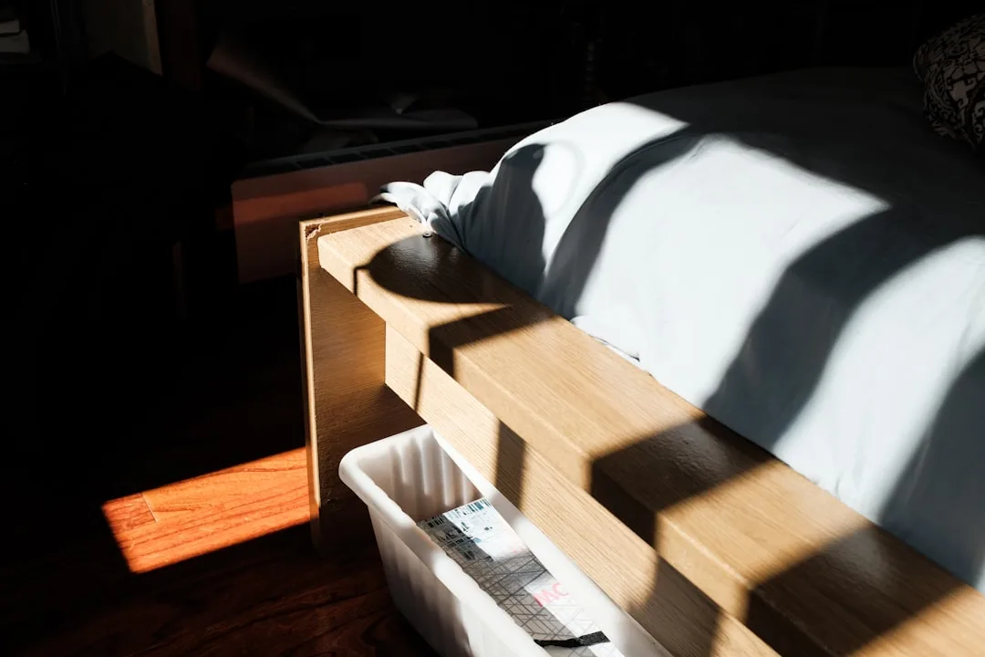 Wooden bed risers elevating a bed frame to increase under-bed storage clearance in a sunlit bedroom