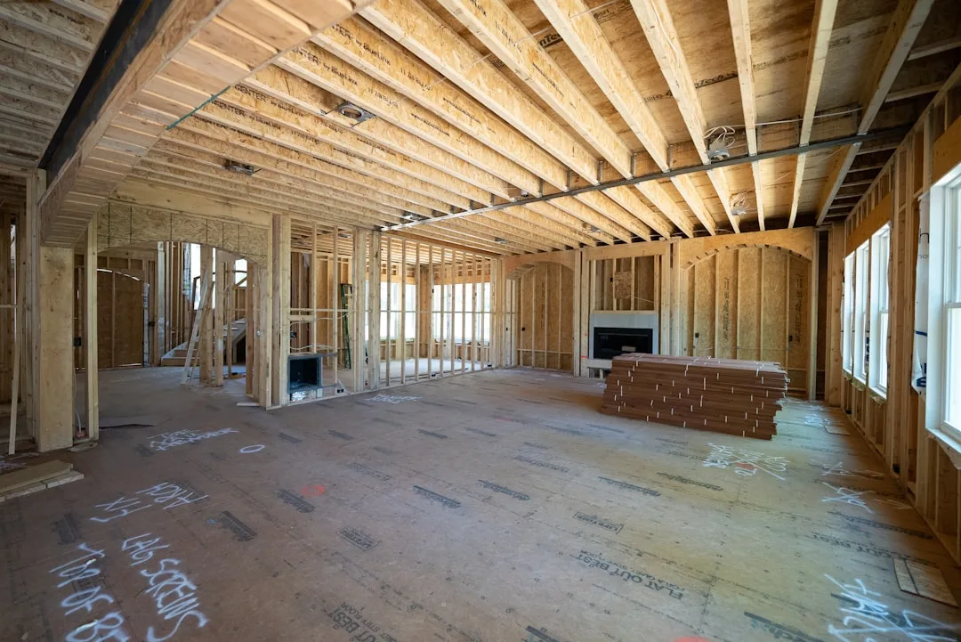 Interior of a house under construction showing wood framing, floor joists, subfloor, and stacked building materials