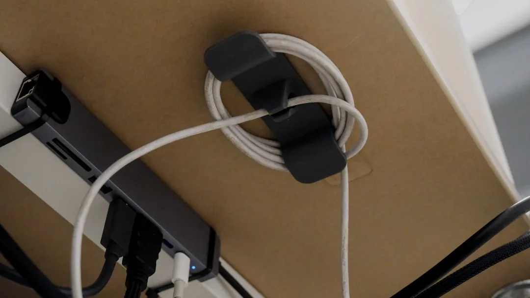 Under-desk cable management with USB hub and coiled white cable holder mounted beneath corner desk surface