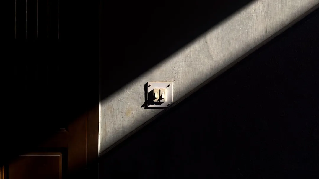 Diagonal shaft of light illuminating a double light switch on a dark textured wall