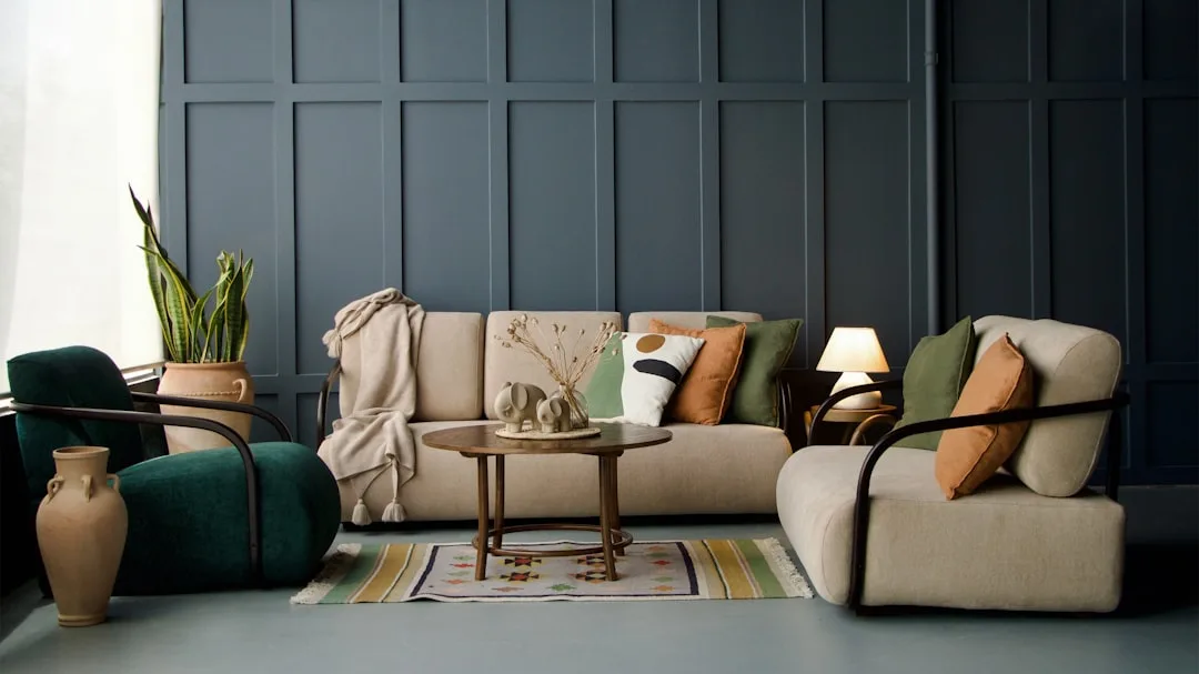 Cohesive living room with beige sofa, green velvet chairs, earth-tone cushions and dark paneled wall showing unified des