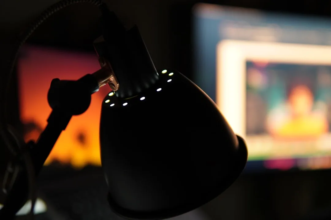 Studio condenser microphone with LED indicator lights in dark home office with monitor display in background