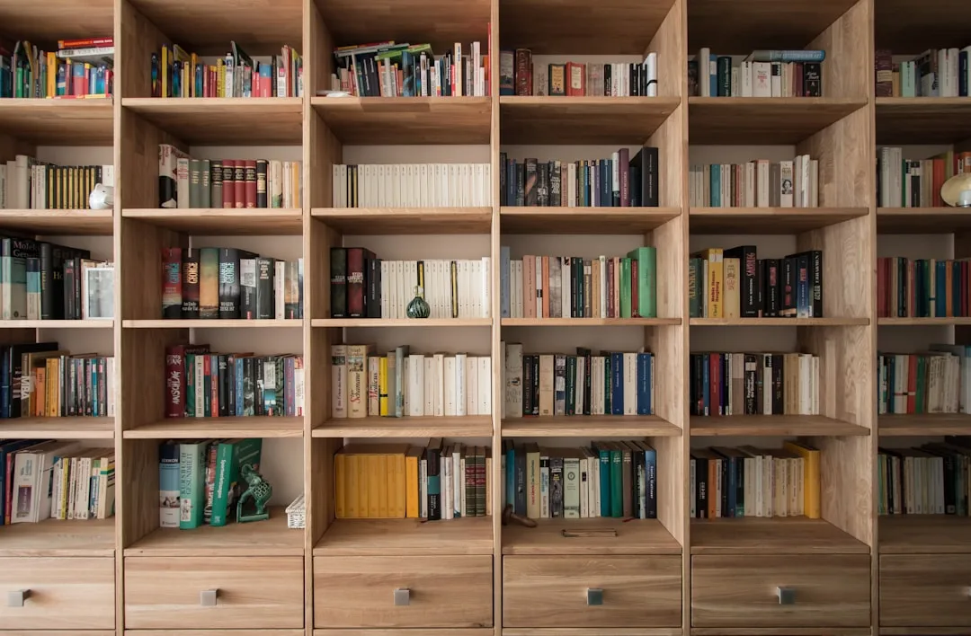 Large wooden bookshelf unit with multiple open compartments filled with books and bottom drawers for storage