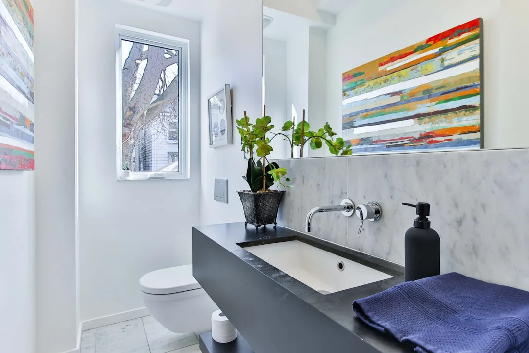 Modern small bathroom with dark vanity, marble backsplash, white walls, and colorful abstract art above sink