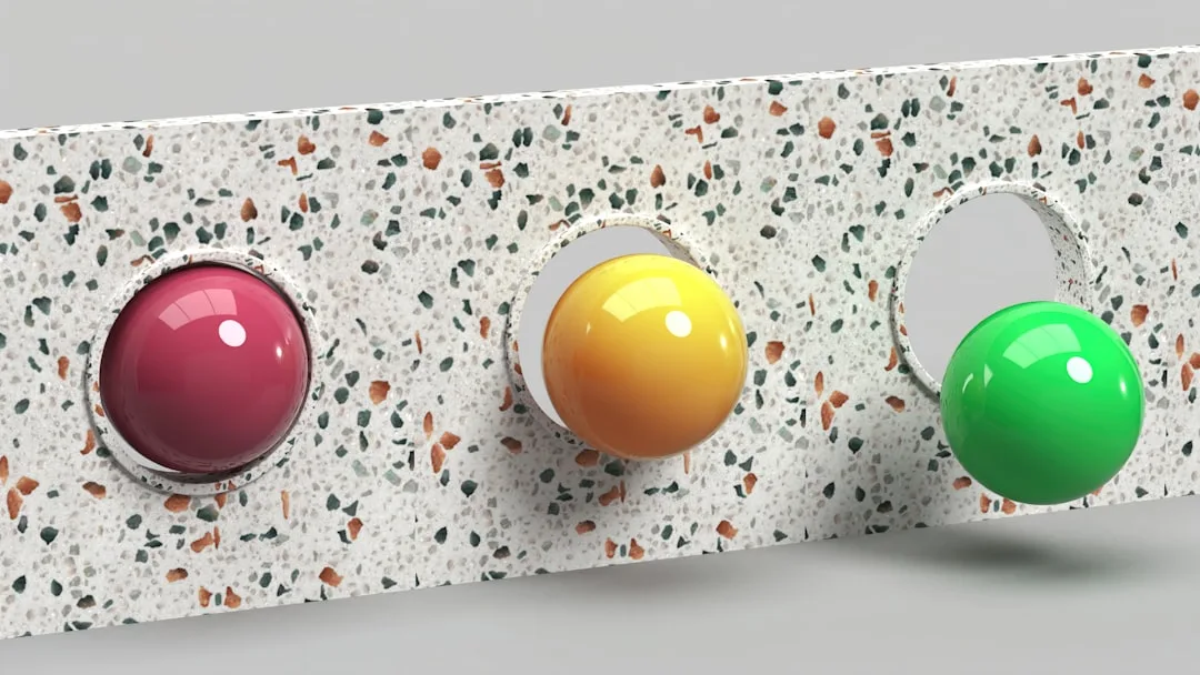 Three glossy spheres in red, yellow, and green mounted on terrazzo surface illustrating color, material, and texture con