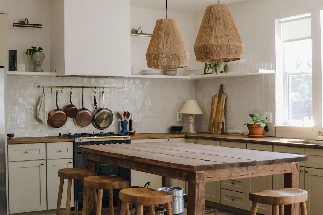 Rustic wooden kitchen island table with stools centered in a small kitchen with woven pendant lights