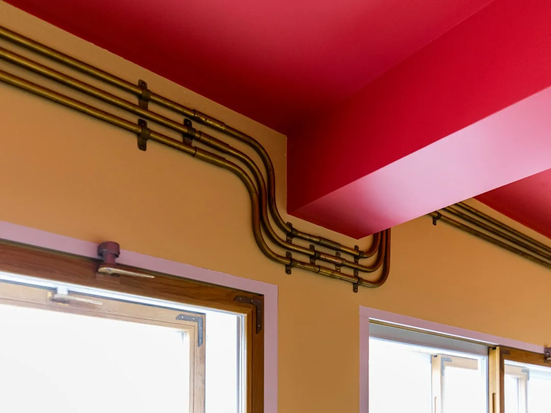 Exposed brass conduit pipes routed along mustard yellow wall near red ceiling, showing intentional wiring detail in inte