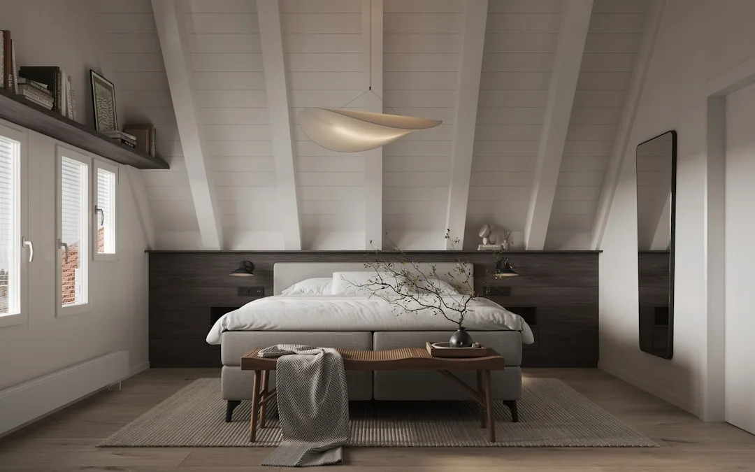 Attic bedroom with sloped white ceiling beams, pendant light, dark wood headboard wall, and natural light from side wind