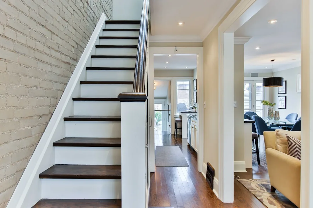 Straight-run staircase with dark wood treads and white risers beside exposed brick wall in open-plan home interior